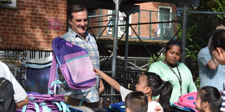 Senator Gianaris hands a young girl a purple backpack