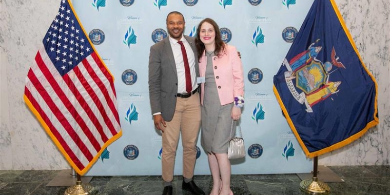 Sen. Jabari Brisport stands with Ms. Abby Stein between a US flag and a New York State flag