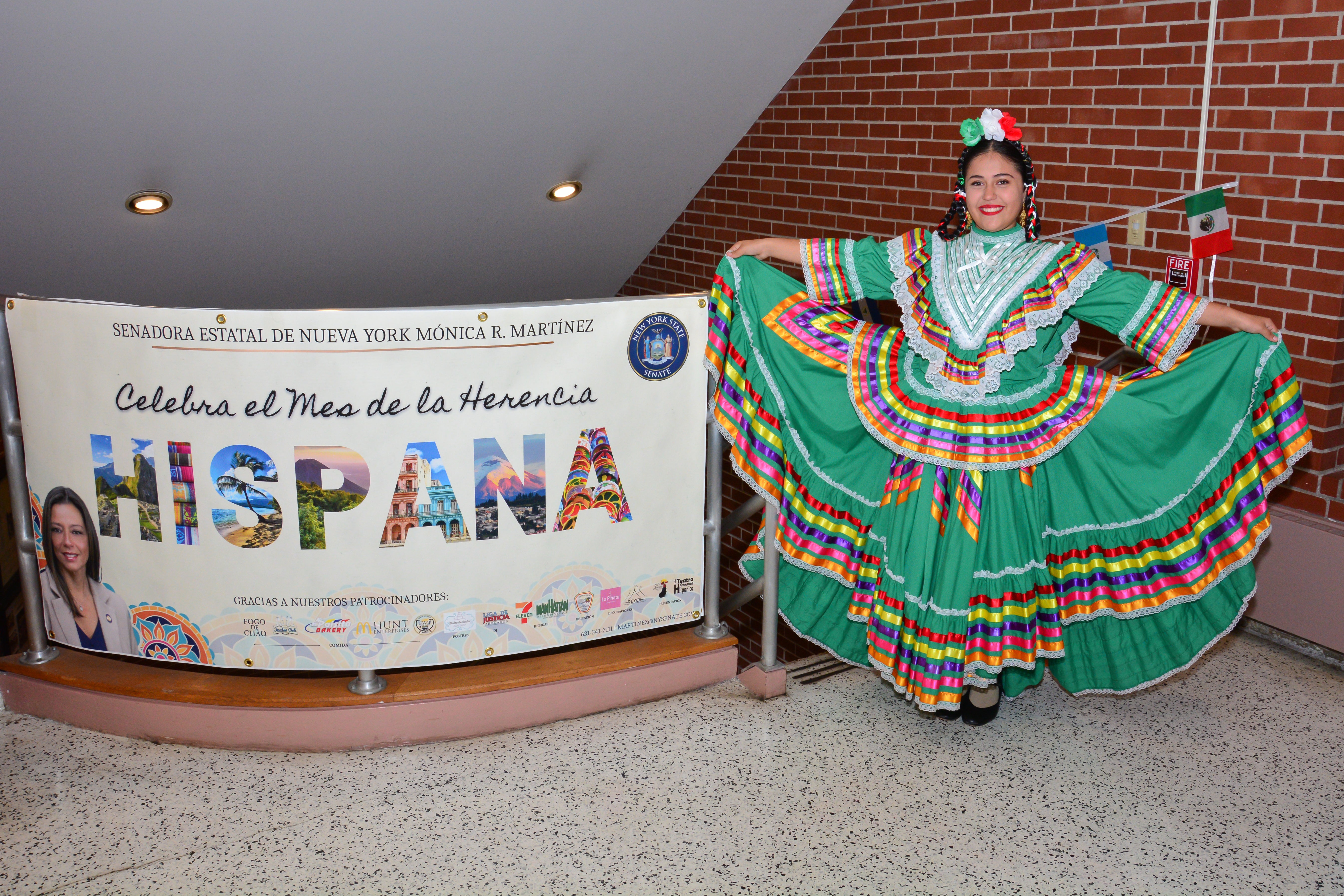 A performer with El Teatro Rodante Hispanico stands with a banner for Sen. Martinez’s Hispanic Heritage Month Celebration.