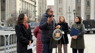 Senator Myrie speaking at a podium in front of the Manhattan Courts