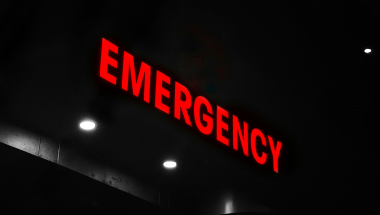 Photo image of an emergency department sign illuminated at night and centered on the word "Emergency."
