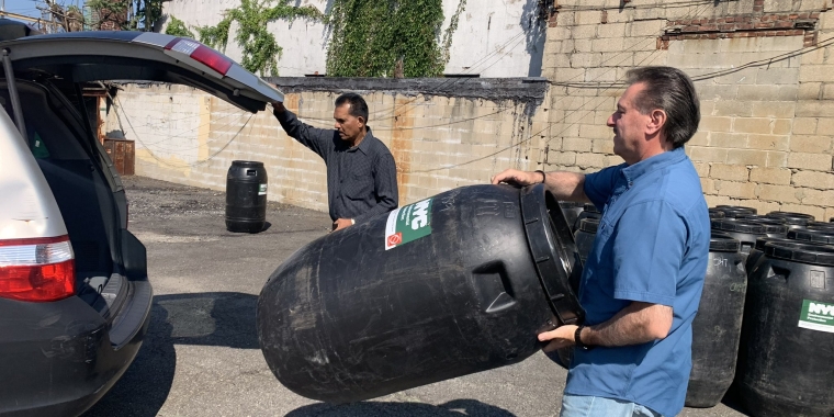 Senator Addabbo helps a constituent load a rain barrel into his car.