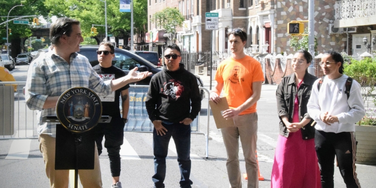 Senator Gianaris at a podium during a press conference standing next to community activists