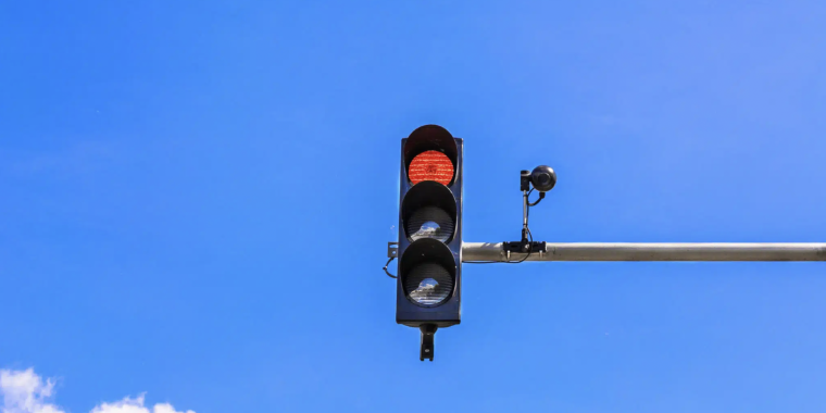 Image of a stoplight with a red light camera attached.