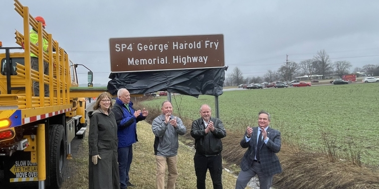 Photo of elected officials and family members in front of highway sign