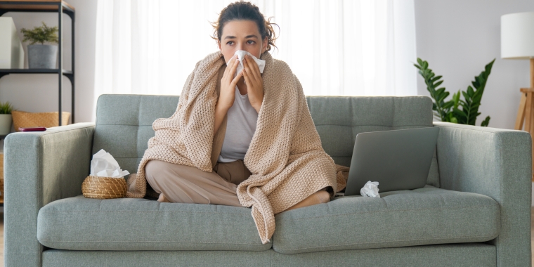 A person sitting on a couch experiencing some of the symptoms of pneumonia.