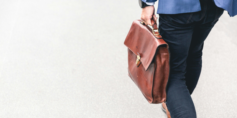 Photo image of the lower half of a person in a suit holding a briefcase while walking. 