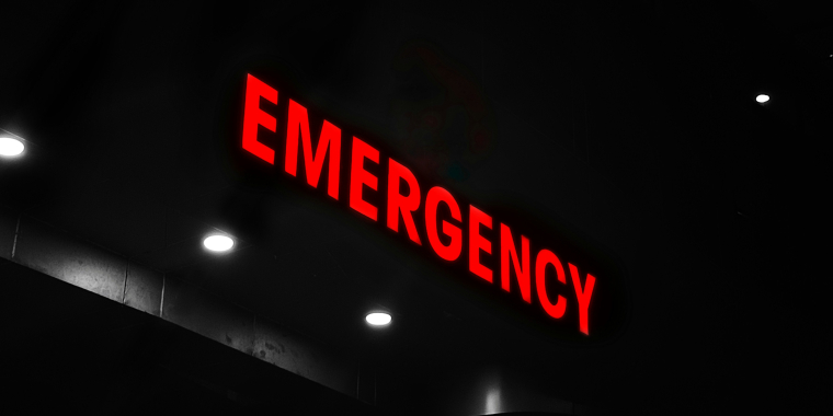 Photo image of an emergency department sign illuminated at night and centered on the word "Emergency."