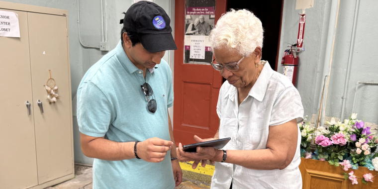 Tyler Singh, the Vice President of DMS International, helps a senior with her tablet at the Ozone Park Older Adult Center.