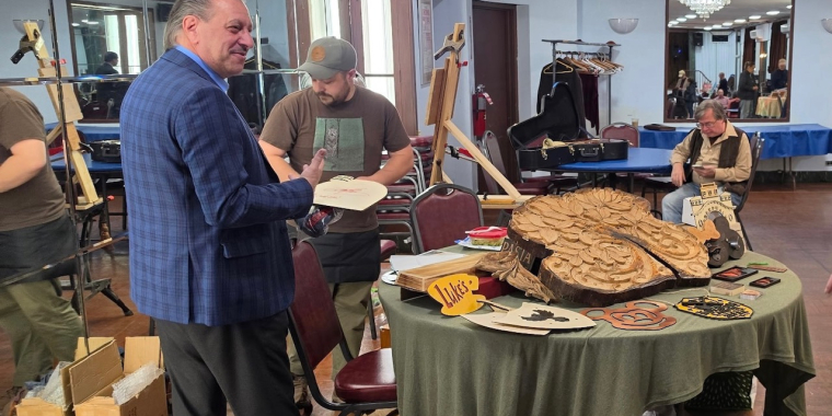 Senator Addabbo admires the work of woodcarver Casey O'Neil.