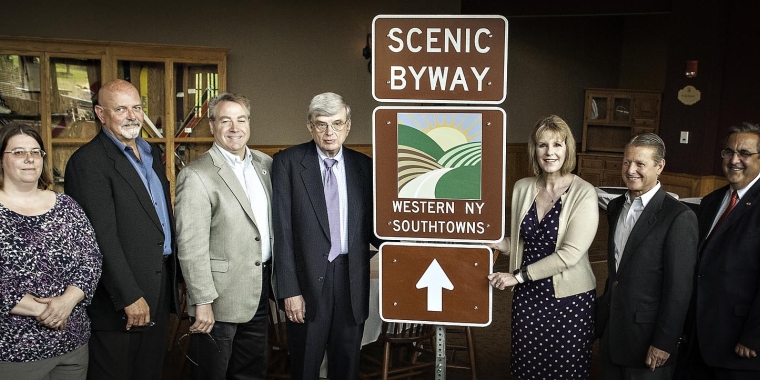 Amy Storer, Resident Engineer for Cattaraugus County, New York State Department of Transportation; Brian McFadden, Executive Director, Ellicottville Chamber of Commerce; Assemblyman David DiPietro; Bob Lennartz, President, Western New York Southtowns Scenic Byway Committee; Senator Catharine Young; Senator Patrick Gallivan; and Assemblyman Joseph Giglio unveil the sign for the Western New York Southtowns Scenic Byway, which has expanded into northern Cattaraugus County.