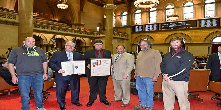In the photo above in the Assembly Chamber on Tuesday, June 4, from left to right: Chris Houseknecht (Dylan’s father), Senator O’Mara, Dylan Houseknecht, Assemblyman Palmesano, Scott Houseknecht (Dylan’s grandfather), and Coach Dan Batchelder.