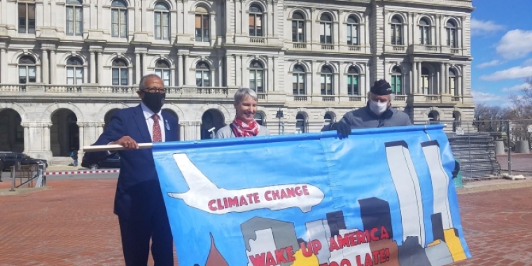 Senator Rachel May and Senator Robert Jackson standing behind a banner depicting the 9/11 terrorist attacks  