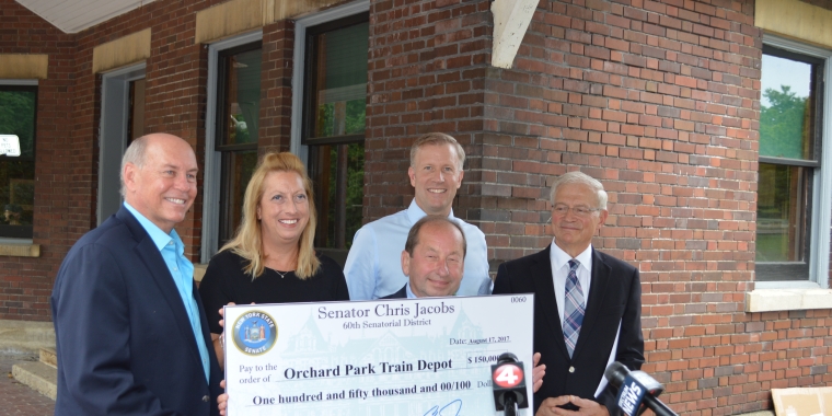 Senator Chris Jacobs is pictured presenting a ceremonial check in the amount of $150,000 for the restoration of the Orchard Park Train Depot to, from L-R, Orchard Park Town Supervisor Dr. Patrick Keem, Village of Orchard Park Mayor Jo Ann Litwin Clinton, Orchard Park Depot Committee Co-Chairman James Slominski and Orchard Park Village Trustee Francis Hogenkamp.